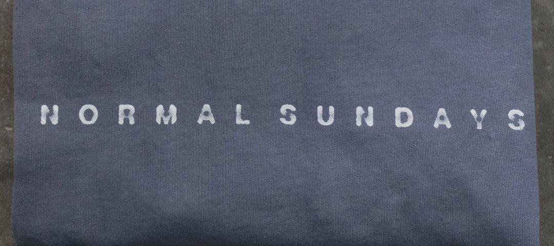 close-up of NORMAL SUNDAYS printed logo on navy garment, representing the brand identity